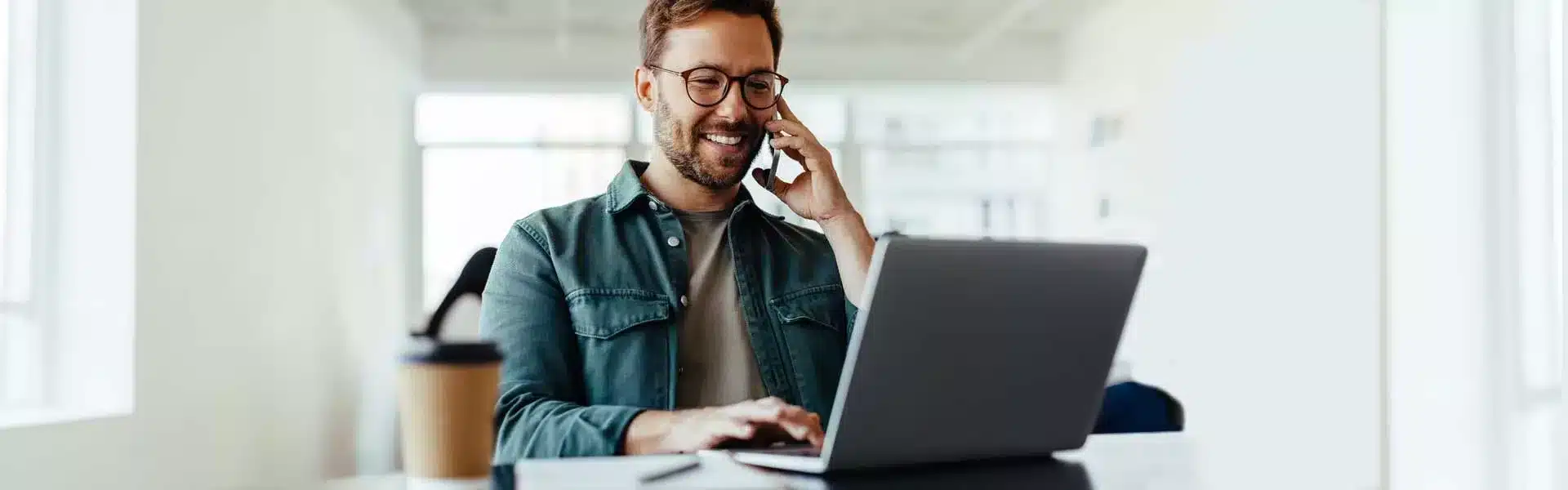 Professionnel en visioconférence depuis son bureau, utilisant un ordinateur portable et son mobile